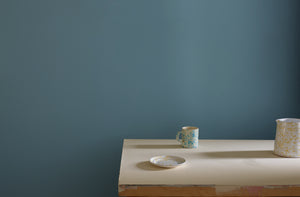 Turquoise and cream splatterware mug and pitcher on a cream surface against a blue wall.