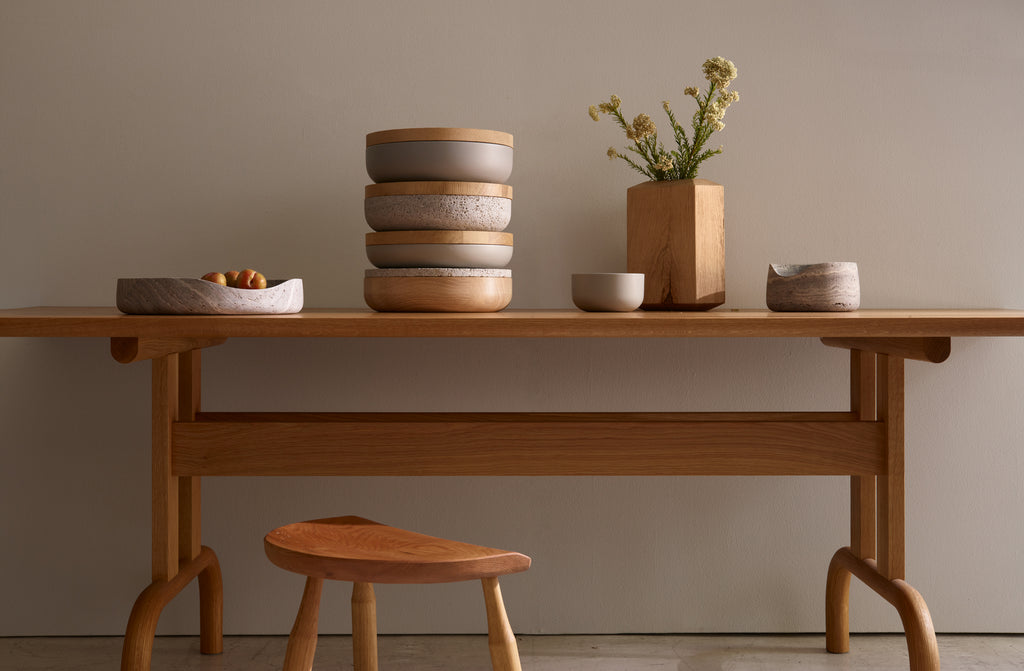 Bowen Liu oak feast table set with Vincent Van Duysen four stacked containers in grey and stone next to an oak Skare vase by Michaël Verheyden and a small and large grey travertine wave bowl by Guillaume Lopez. Default