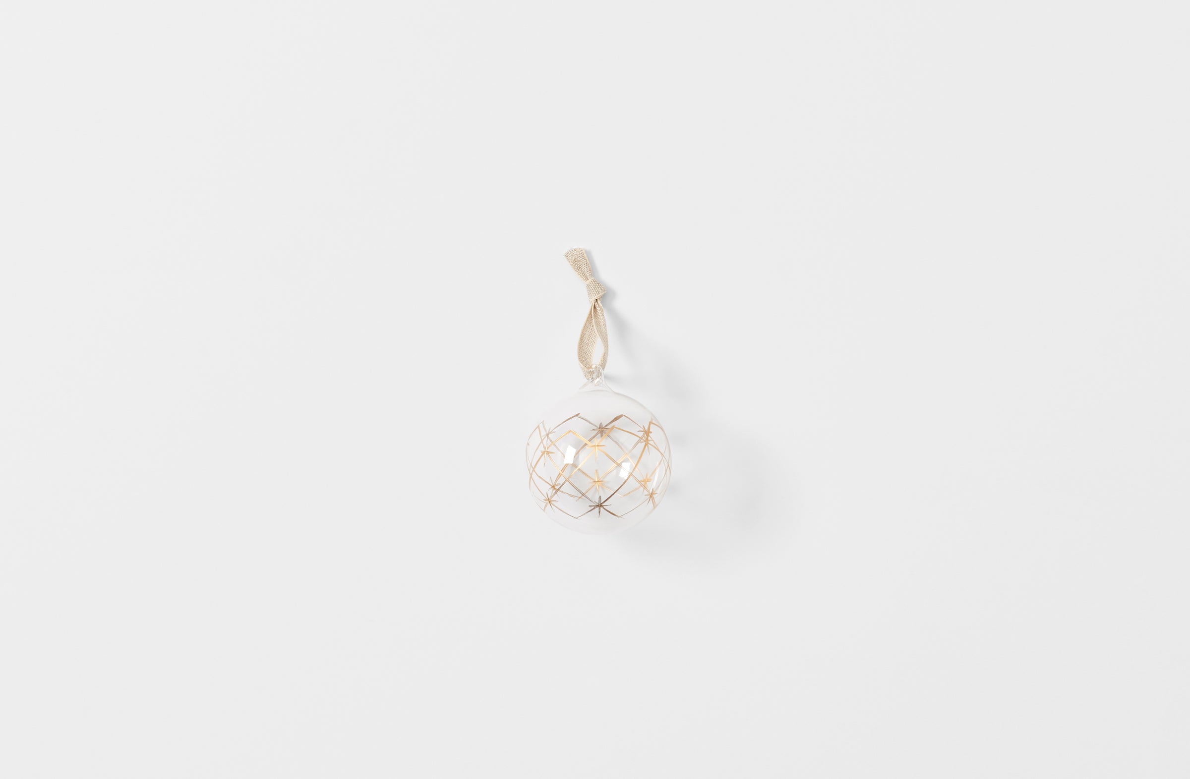 Clear glass ball ornament with gold star pattern strung with linen tape