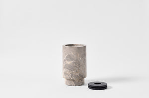 Michael Verheyden grigio carnico marble vase with leather lid removed and sitting next to it.