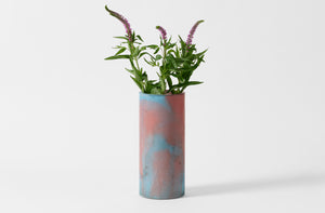 Turquoise and rust Michael Verheyden concrete vase holding purple flowers.