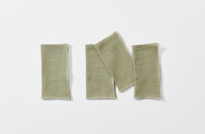 Four folded moss linen napkins with natural rolled edge.