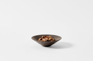 Shallow black Takashi Endo bowl holding unshelled pecans.