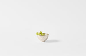 A Takashi Endo silver bowl holding green grapes on white background.