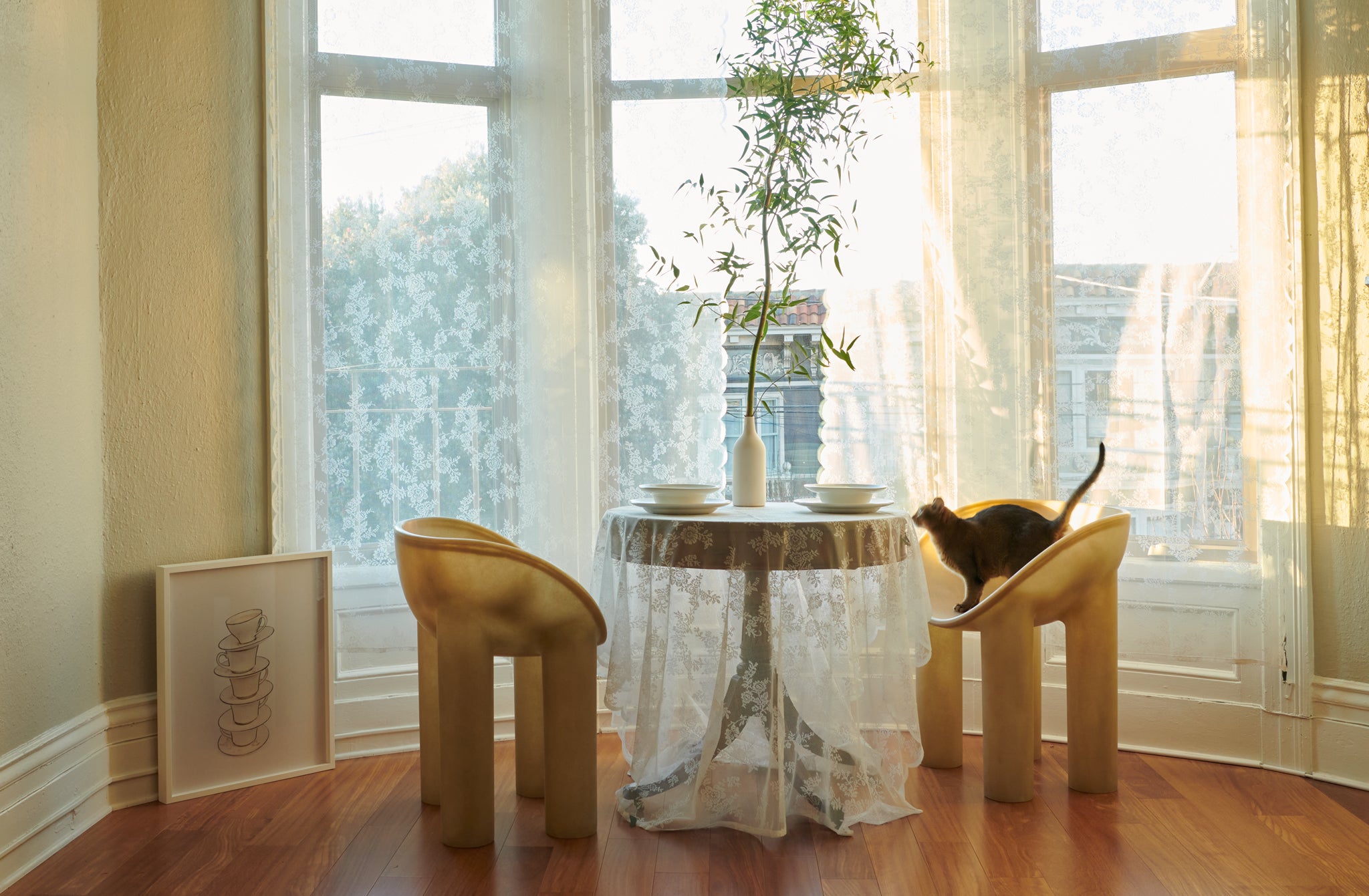 Bay-Window-with-Antique-Table-set-with-Tracie-Hervy-porcelain-bottle-vase-and-john-julian-dinnerware-with-Two-Faye-Toogood-Roly-Poly-Raw-Dining-Chairs-one-with-a-cat-standing-inside-and-looking-at-table-setting-Insitu-MARCH