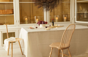 At-MARCH-simple-holiday-table-set-with-cream-and-pale-wood-accents-with-Sawyer-made-windsor-chair-and-faye-toogood-ash-spade-chair-and-candlelight-behind