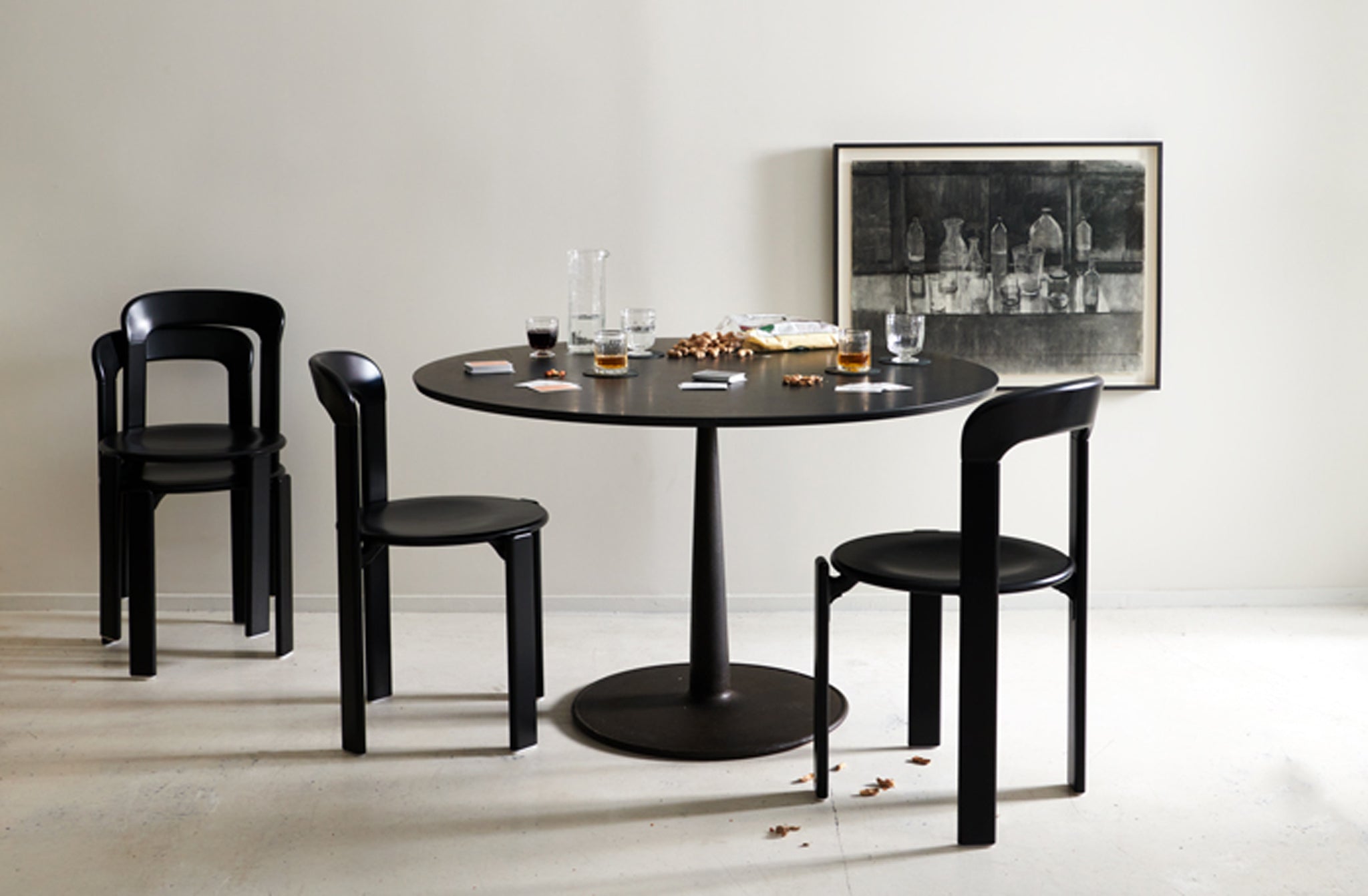 MARCH-joshua-vogel-marble-and-cast-iron-table-with-bruno-rey-black-chairs-set-for-a-card-game-with-jason-line-framed-drawing-of-glassware-hanging-behind