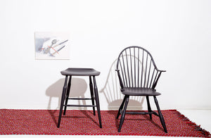 At-MARCH-sawyer-made-widsor-arm-chair-and-hunter-stool-in-black-milk-paint-atop-braided-red-rug-with-carriemae-smith-painting-on-wall-behind