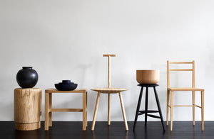 At-MARCH-row-of-oak-and-ash-stools-and-chairs-with-black-accessories-including-faye-toogood-ash-spade-chair-michael-verheyden-oak-stools-and-sawkille-drink-stool