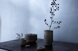 michael verheyden brown travertine vases in three sizes two set with tonal branch on an antique table with a dark silver background