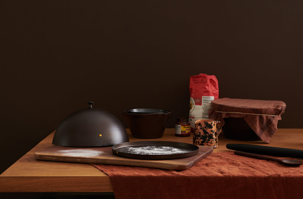 Baking-scene-with-baking-cloche-mixing-bowls-and-wooden-tools-atop-worktable-Default