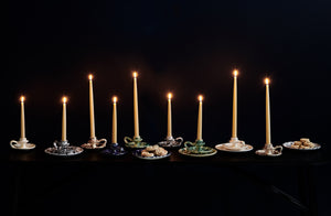 multi colored splatterware candlesticks with lit taper candles enmasse against a dark background