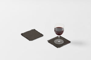 boxwood dark grey belgian linen square coasters with a fringe edge shown with one goblet of red wine atop one coaster