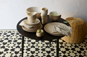 Brickett Davda dinnerware stacked on Sawkille ebonized table on graphically patterned floor. Default