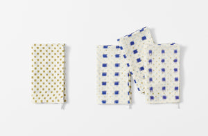 four folded gregory parkinson indigo square napkins with one napkin folded to the reverse pattern of small khaki squares on cream