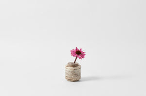 michael verheyden brown travertine petite vase shown with one pink dahlia